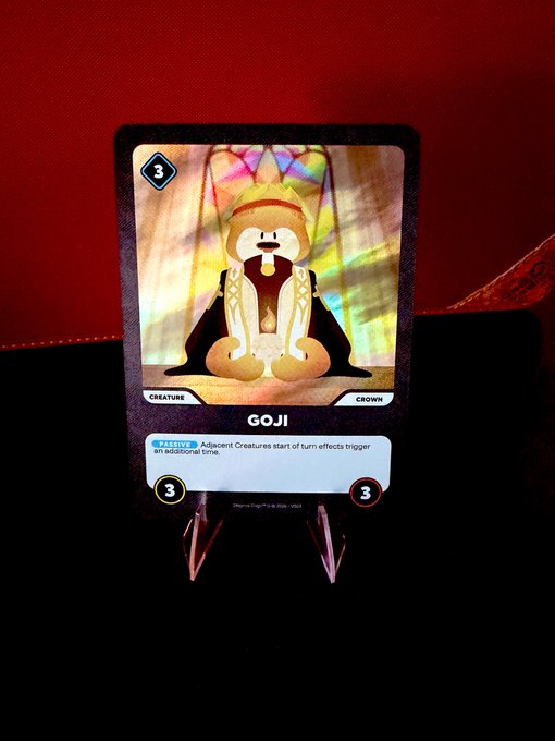 A holographic Pokémon trading card named 'GOJI' sits on a clear stand against a red background; it is a 'Creature' and 'Crown' card with a cost and power of 3, and an ability called 'Light Up'.