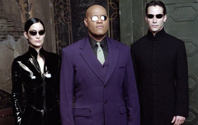 The image features three figures in dark, sleek attire and sunglasses, including a central man in a purple suit, evoking a sci-fi secret agent aesthetic. It likely illustrates the post's metaphor of an "agent" acting with seamless autonomy, paralleling how the $Wire control layer abstracts away infrastructure complexity to let agents focus solely on outcomes.
