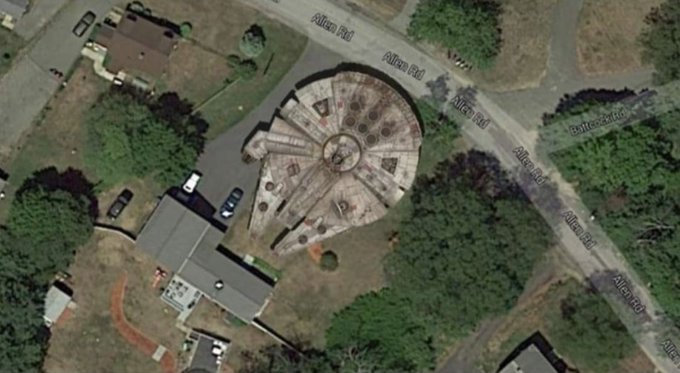 Aerial satellite view of a circular building with a radial spoke pattern on its roof, surrounded by trees and Allan Rd.