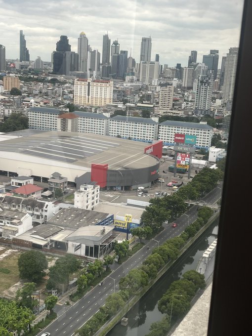 An aerial city view from a high-rise window overlooks a dense urban area with visible signage including "Lotto," "The Mall," and red banners, possibly indicating a vibrant shopping district. The hazy skyline features tall skyscrapers in the distance, suggesting an impending visit with Grandma Luna.

**Wait** — the post references "Luna" and uses the hashtag "#Lunar," not a person named Luna. Combined with the hazy/overcast atmosphere visible in the image, the caption likely plays on this lunar/celestial aesthetic rather than referring to a grandmother. A more fitting caption: An overcast aerial cityscape with distant skyscrapers and a commercial district featuring "Lotto" and "The Mall" signage, matching the moody, muted atmosphere of the #Lunar post.