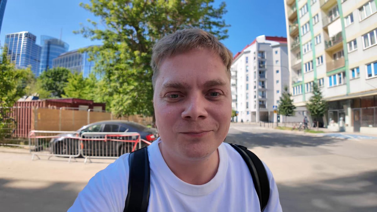 The image features a man wearing a white shirt, standing outdoors with his face towards the camera. He has a backpack on his back and appears to be smiling for the photo. The background of the image shows buildings, suggesting that he might be in an urban setting or near a construction site. The caption "This is actually one of the best BuildInPublic series on @solana" implies that there could be more information about this particular post available if desired.