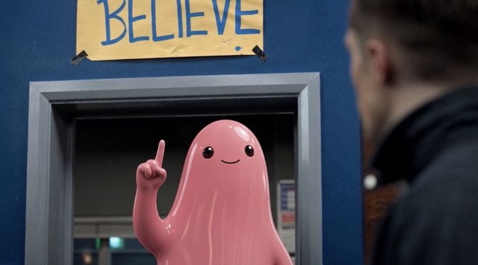A pink ghost-like figure points upward in front of a doorway under a 'BELIEVE!' sign, while a man stands in the foreground facing away.