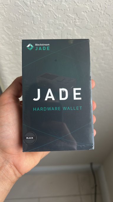 A hand holds up a black box for a 'Blockstream JADE HARDWARE WALLET' in BLACK color.