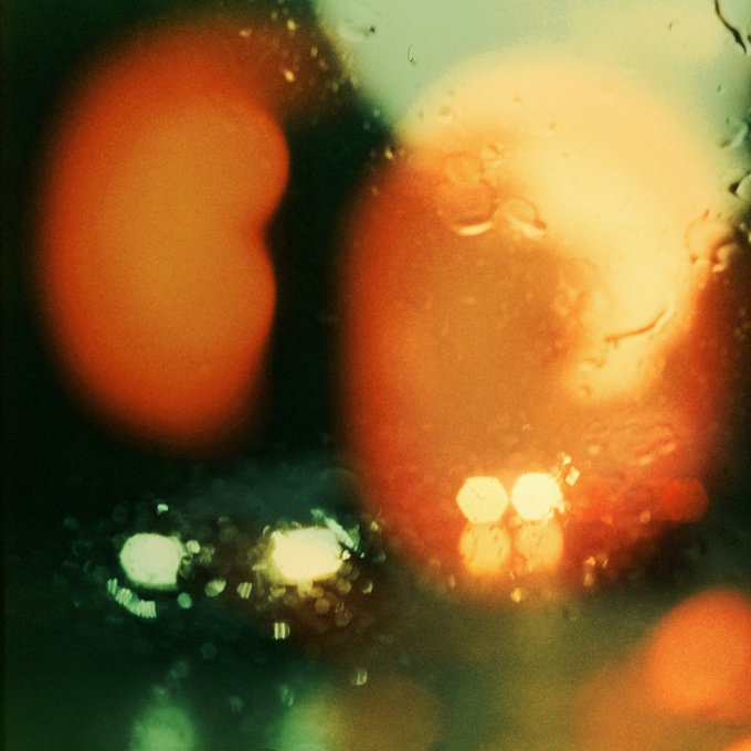 A blurry, vintage-style photograph showing orange light orbs or bokeh effects against a dark green and black background.