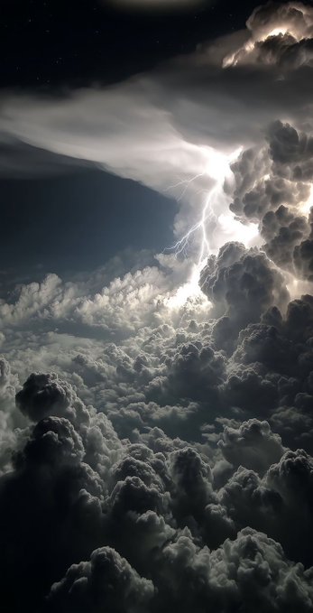 A dramatic black and white photograph captures lightning striking through towering cumulonimbus clouds at night.