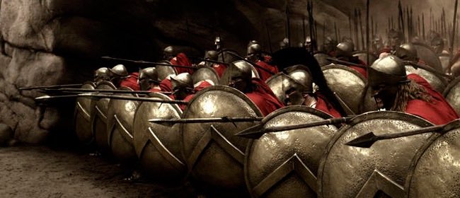 A phalanx of Spartan warriors, locked shoulder-to-shoulder with shields raised and spears pointed forward, stands ready as a powerful metaphor for the collective bearish pressure on $BTC defending the $65,500 support level.