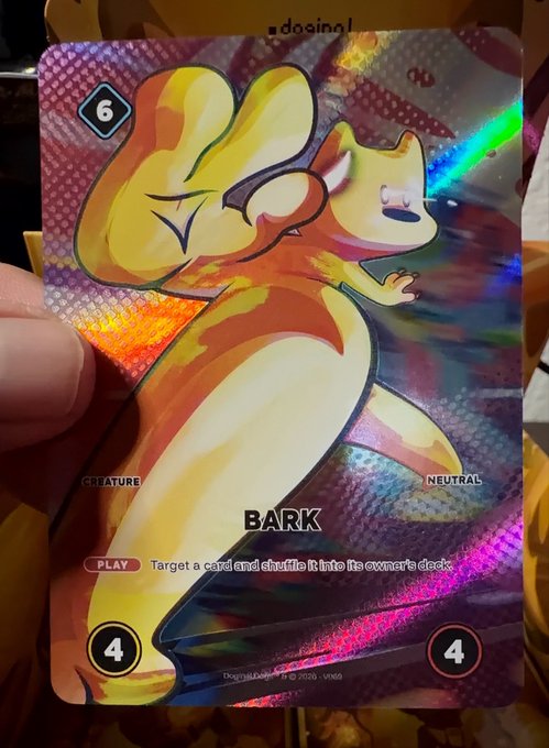 A hand holds a holographic trading card featuring a yellow fox-like creature named "BARK," with stats of 6, 4, and 4, and gameplay text "Target a card and shuffle it into its owner's deck."