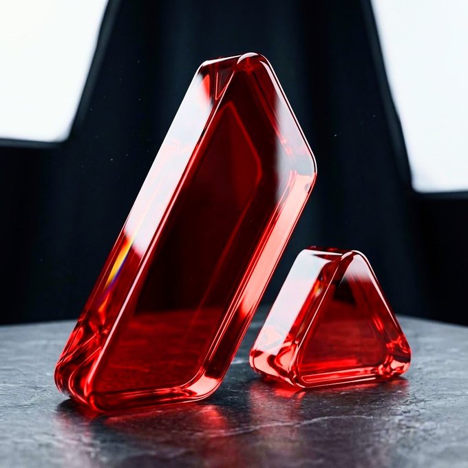 Two translucent red geometric objects, one larger triangular prism and one smaller triangular pyramid, displayed on a dark surface with dramatic lighting.
