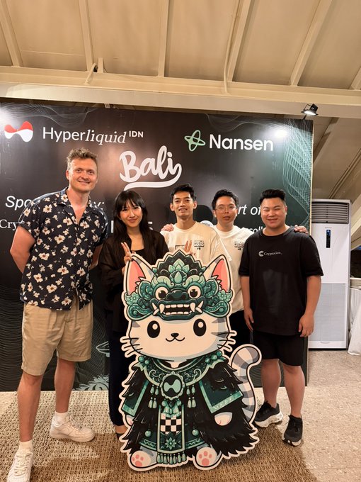 A group of five people poses with a cartoon cat mascot in traditional Balinese attire at the Hyperliquid Bali event, with a backdrop featuring "HyperLiquid IDN," "Nansen," and "Bali" branding. The image captures the first HyperliquidX Bali gathering, showcasing community members connecting at what appears to be a sponsored meetup.