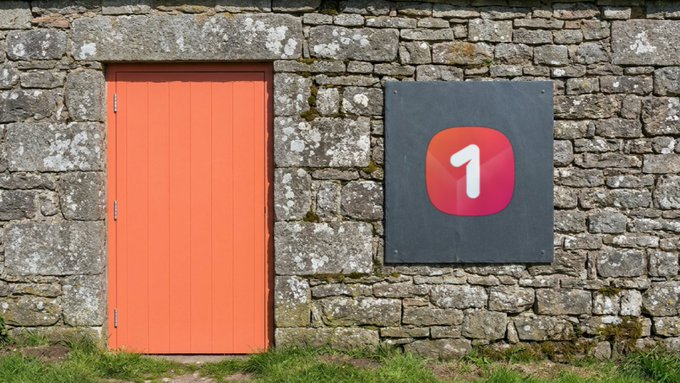 A coral-orange wooden door is set into a weathered stone wall beside a sign displaying the "1" logo of ONEstore, the game platform referenced before its blockchain transition. The rustic exterior contrasts with the modern branding of what was once a mobile gaming marketplace.
