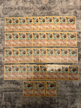 The image shows a collection of Pokemon cards neatly arranged on a gray surface, with each card facing the same direction. There are a total of 16 cards visible, spread across the entire width of the image. The cards appear to be of various sizes and colors, indicating that they might be from different series or releases. The arrangement suggests that these cards could be part of a collection or a display for others to admire.