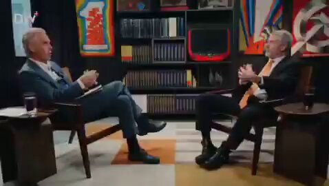The image shows two men sitting across from each other in chairs while one man holds a book. The background features several bookshelves filled with various books. The caption reads "MICHAEL SAYLOR: IF QUANTUM COMPUTING HACKS YOUR EMAIL, DOES IT BREAK THE ENGLISH LANGUAGE?", which is related to the post about Bitcoin and its relation to engineering principles.