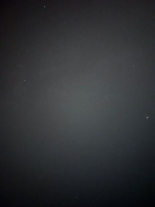 A dark, low-light photograph of a night sky with scattered, faint stars.