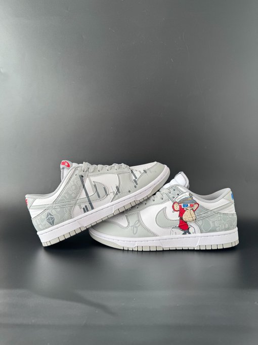 A pair of grey and white Nike Dunk Low sneakers featuring a graphic monkey mascot and star patterns, displayed against a dark grey background.