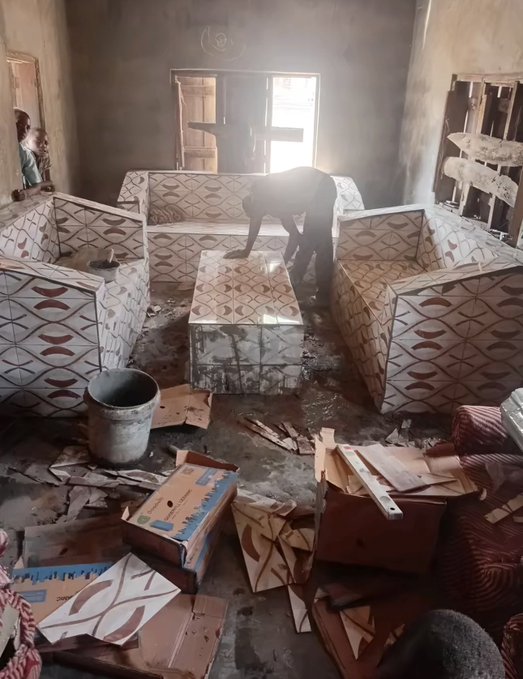 A worker applies adhesive to patterned sofa pieces in what appears to be an upholstery workshop, surrounded by various furniture components and tools.
