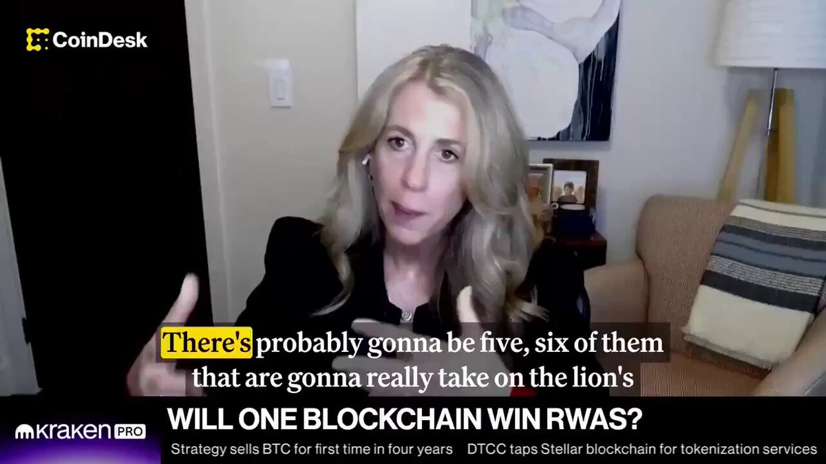 The image features a woman with blonde hair sitting in a chair, wearing a black outfit. She appears to be giving a speech or participating in an interview. The background of the image shows a wall clock and a couch, suggesting that she might be in someone's living room. There is also text on the image that reads "There's probably gonna be 5-6 RWA chains will emerge i tend to agree come to $MANTRA for compliant RWA finance". This statement seems to be related to the woman's speech or interview about cryptocurrency and blockchain technology, as she might be discussing the potential growth of RWA chains in the future.