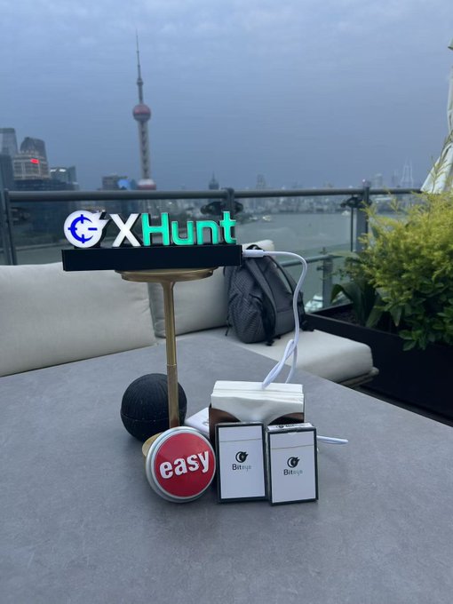 A promotional photo for 'GXHunt' showing branded merchandise (a sign, an 'easy' pin, and small boxes) on a table overlooking the Shanghai skyline, including the Oriental Pearl Tower.