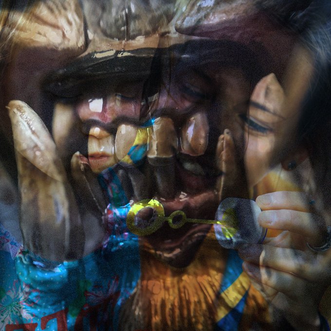 A dreamlike double-exposure of two figures interacting with glowing bubble-blowing toys, the translucent spheres refracting fragmented facial features and colorful patterns across the frame—evoking the experimental, disorienting aesthetic of the album cover for "Amnesia Scanner & Bill Kouligas – Lexachast" on PAN Records.