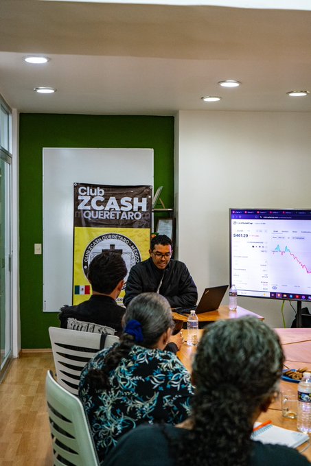 A photograph of a presentation at 'Club ZCASH QUERÉTARO', showing a man at a laptop with a large screen displaying a Zcash price chart of $461.29, with several audience members seated at a table.
