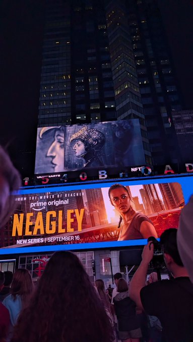 A nighttime view of large billboards in a city, including one for a new series titled 'NEAGLEY' premiering September 16.