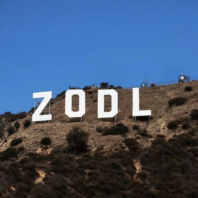 Large white letters spelling 'ZODL' are displayed on a dry, brush-covered hillside under a clear blue sky.