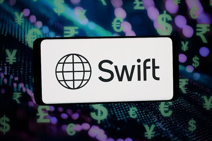 A white smartphone displaying the 'Swift' logo (globe icon) against a digital background of colorful floating currency symbols including yen, dollar, euro, and pound.