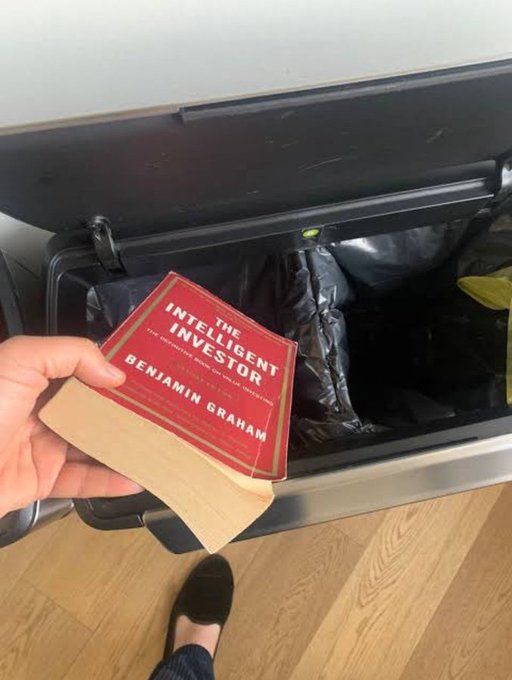 A hand holds a paperback copy of Benjamin Graham's "The Intelligent Investor" above an open trash bin, implying the book itself is being discarded—an ironic visual contrast to the social media post claiming someone turned $2K into $1M, which ironically sells what Graham's classic value-investing book actually teaches.
