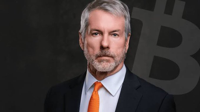 Michael Saylor, executive chairman of MicroStrategy, is shown in a formal portrait wearing a suit and orange tie, with a faint Bitcoin (₿) symbol displayed in the background—visually reinforcing his advocacy for Bitcoin as highlighted in the accompanying quote about transforming economic value into secure digital form.