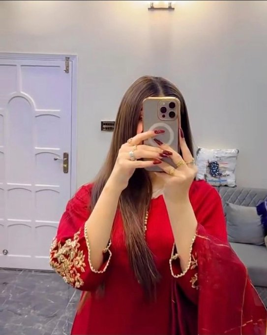 A mirror selfie of a woman in a red embroidered traditional-style outfit holding an iPhone with a gold case, wearing several rings.
