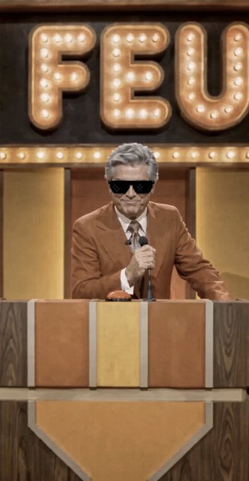 A man wearing sunglasses and a brown suit speaks at a podium beneath large illuminated letters spelling 'FEU'.