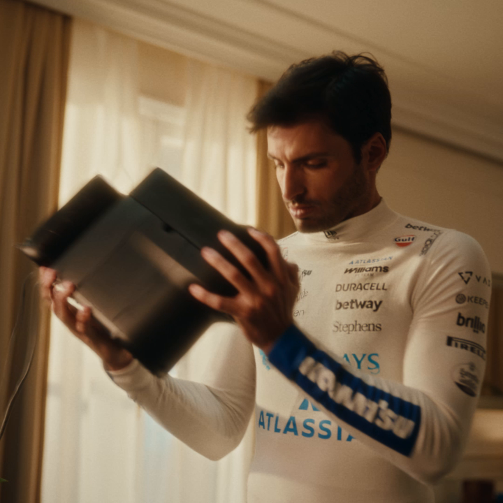 A Williams Racing team driver in a white firesuit featuring sponsor logos (ATLASSIAN, DURACELL, betway, Stephens) intently examines a black object, with the post linking to "@WilliamsF1" to promote a smoother approach to investing.