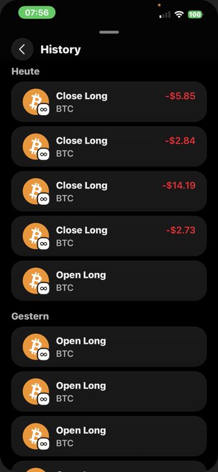 The image shows a black cell phone screen displaying a list of Bitcoin trading options, including "Open Long" and "Close Long", along with their respective prices. The text on the screen reads "History", "Heute", "Close Long", and "OPEN LONG". The phone is positioned in such a way that it appears to be turned off or not actively displaying any content at the moment.