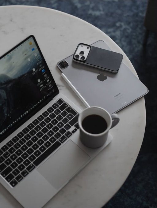 An overhead view of a white marble table holding an open MacBook Pro, two iPhones (one in a gray case), and a white mug of coffee.