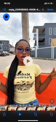 A woman wearing an "Adam & Eves" t-shirt speaks to the camera while eating something, gesturing as she discusses ProphetMarketAI, where an AI-powered House serves as the counterparty in prediction markets instead of another trader.