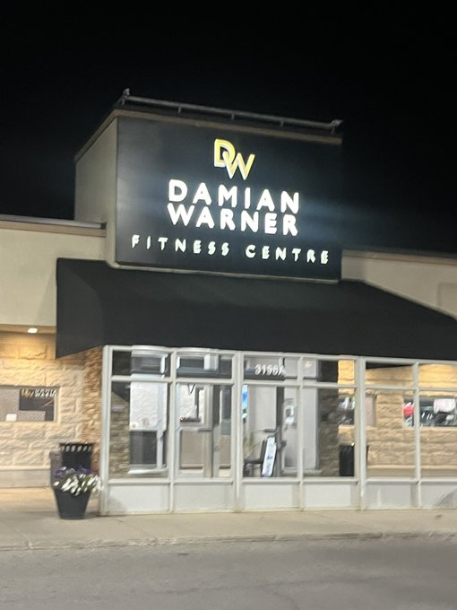 An illuminated nighttime exterior shot of 'Damian Warner Fitness Centre' with its 'DW' logo.