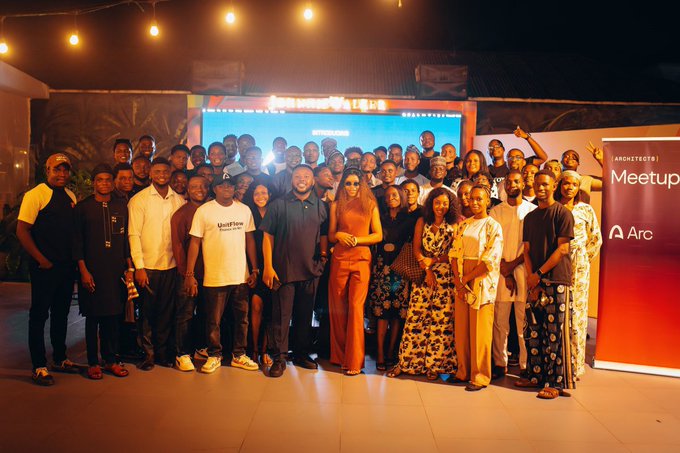 Group photograph of attendees at an 'Architects Meetup' hosted by Arc, taken indoors with warm string lighting and a branded banner visible on the right side.