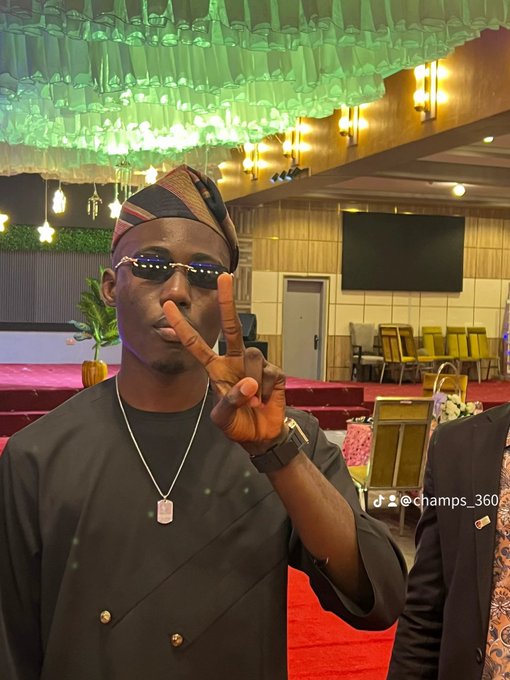 A man in sunglasses and traditional black attire with a "Fila" cap flashes a peace sign at what appears to be a formal event venue, with the Instagram handle "@champs_360" visible. The caption "gm 𝕏 mutuals. Let's focus on the bag .." suggests he's showcasing his stylish outfit and accessories to his social media community.