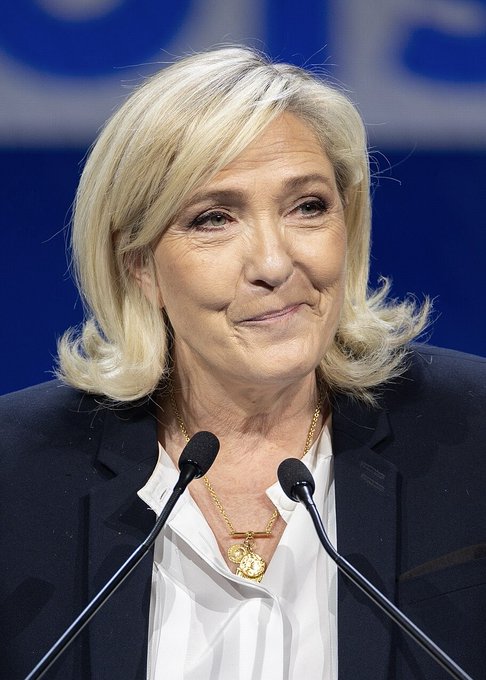Marine Le Pen, leader of France's National Rally party, is shown here at a podium with microphones, looking composed with a slight smile as she emerges as the betting favorite to win France's 2027 presidential election with 38% odds.