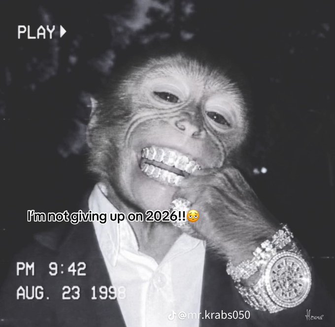 A black-and-white VHS-style image shows a photoshopped monkey face on a body wearing a suit and an icy diamond watch, with overlays reading "PLAY ▶," "PM 9:42," "AUG. 23 1998," and "I'm not giving up on 2026!!😩," watermarked "@mr.krabs050." The retro, late-night "locked in" vibe of the meme ties into the post's "We locked in regardless" energy, playfully suggesting determination and resilience heading into the new year.