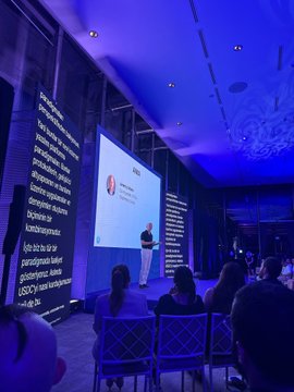 A dimly lit conference room bathed in blue light where a speaker presents on a screen displaying 'USD Coin enterprise,' with text on the side wall referencing 'global stablecoins.'