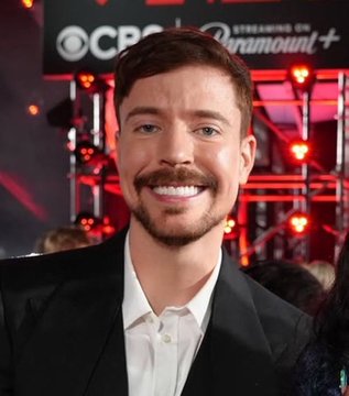 A man with a trimmed beard and mustache smiles in a black suit and white shirt, standing in front of a backdrop featuring CBS and Paramount+ logos. The image is being used to falsely associate the man with a cryptocurrency presale scam claiming to be connected to MrBeast.