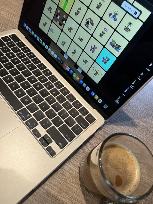 A MacBook displays a grid of pixel-art NFTs on its screen next to a frothy coffee mug on a wooden desk, capturing a cozy Friday morning setup perfect for trading crypto collectibles.