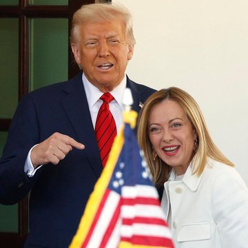 Donald Trump stands next to Giorgia Meloni, who is smiling, with an American flag in the foreground.