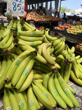 Bunches of Dole bananas with stickers are displayed at a market, with a price sign showing "85¢/lb" and other produce like apples and oranges visible in the background—pairing perfectly with the "good morning" post suggesting buying fruit as a friendly gesture.