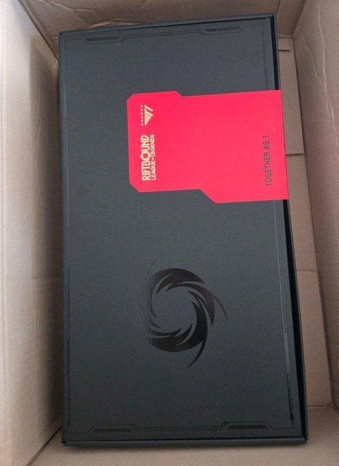 A black 'REBOUND - RAGE AGAINST-' branded box with a red card labeled 'TOGETHER AS 1' and a spiral logo, sitting inside a brown cardboard shipping box.