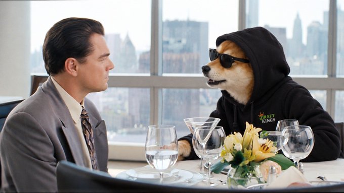 Humorous edited image styled like a movie scene (resembling 'The Wolf of Wall Street'), showing Leonardo DiCaprio in a suit sitting across from the Doge/Shiba Inu meme dog wearing a black 'DRAFTKINGS' hoodie and sunglasses at a fancy restaurant.