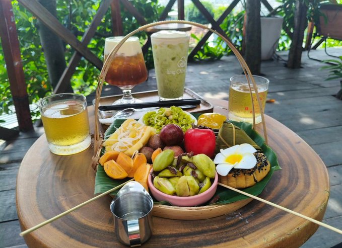 A tropical fruit platter served in a bamboo basket on a wooden table, accompanied by glasses of iced coffee and tea.