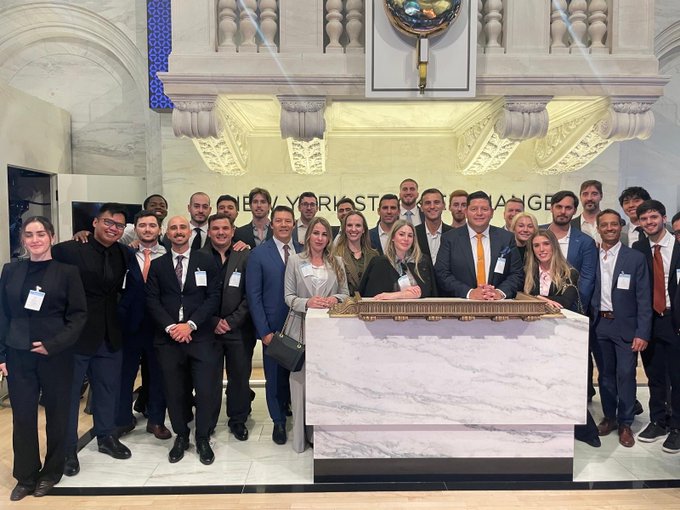 A group photo of professionals in business attire gathered around a marble podium at the New York Stock Exchange, marking a corporate milestone or IPO event.