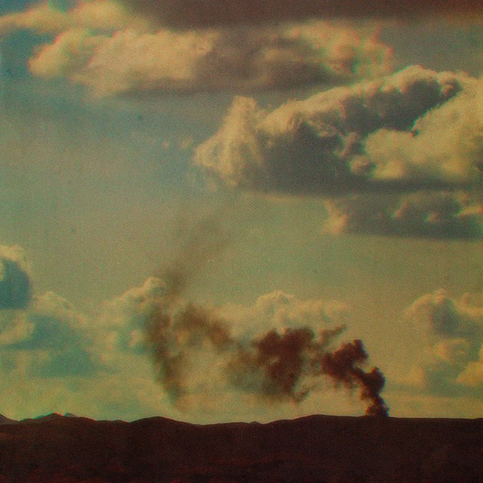 Smoke rising from a distant landscape under a cloudy sky, captured with a vintage, faded film aesthetic.