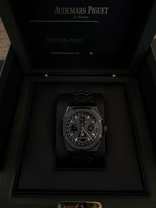 A black Audemars Piguet Royal Oak Perpetual Calendar watch sits in a black presentation box alongside an "AUDEMARS PIGUET INTERNATIONAL WARRANTY CARD."